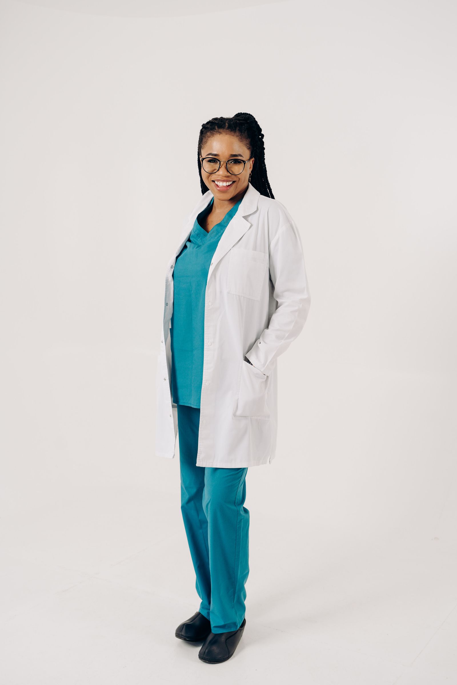Confident female doctor smiling, wearing scrubs and a white coat with a professional pose.