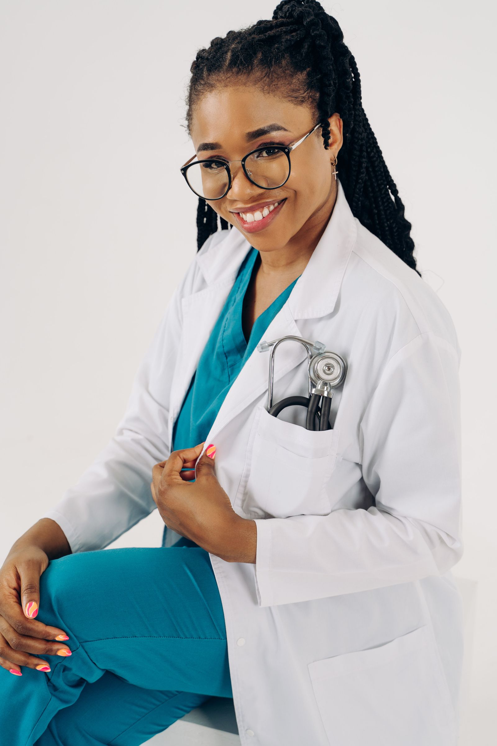 Confident female doctor in white coat and glasses, sitting with a smile.