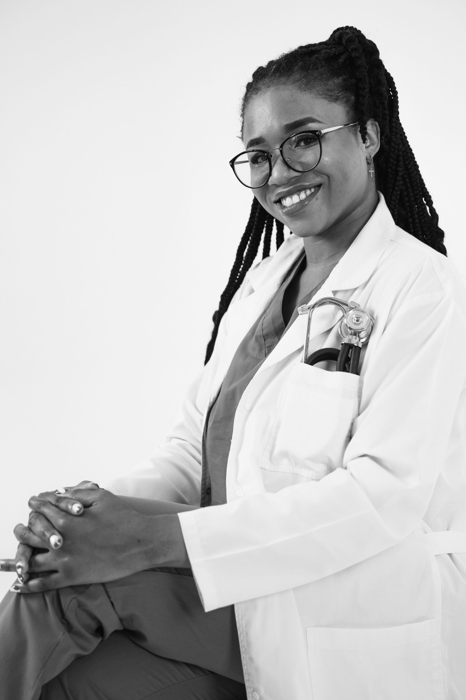 Portrait of a confident female doctor smiling, wearing eyeglasses and a lab coat in black and white.