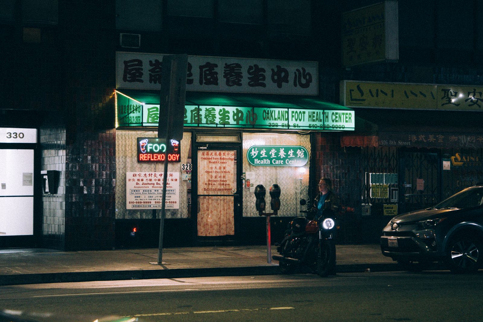 A nighttime view of a foot health center in Oakland's Chinatown with a person beside a motorcycle.
