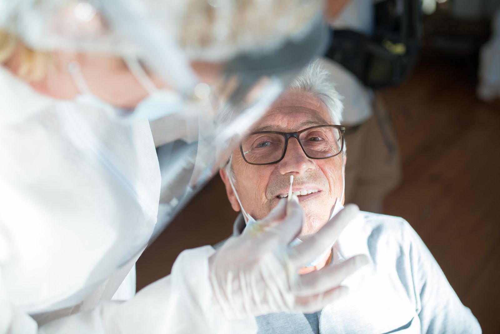 Elderly man receiving a nasal swab test from a healthcare professional in a clinical setting.